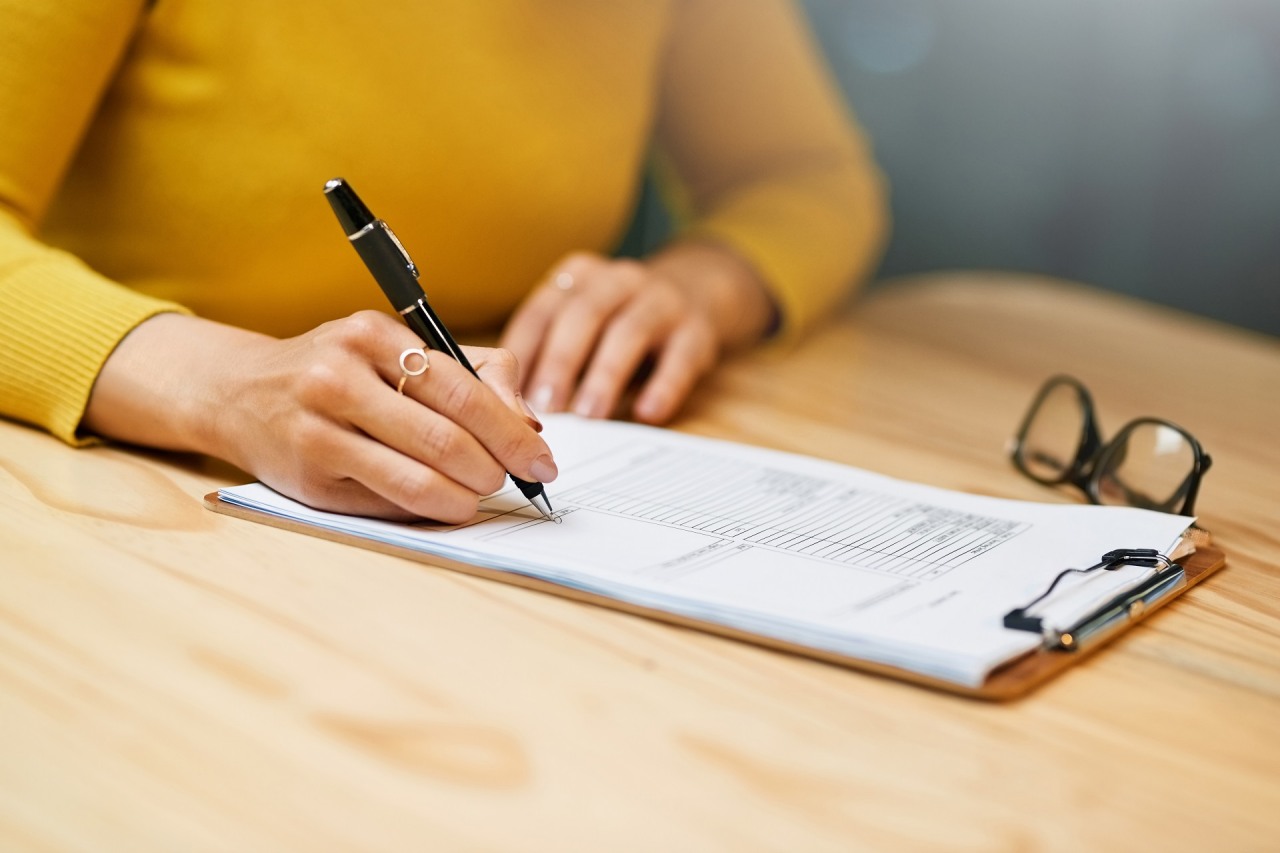 Closeup shot of an unrecognizable woman filling in paperwork on a clipboard at a table